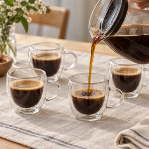 Café sendo servido em uma das quatro xícaras de vidro transparente com alça à mesa