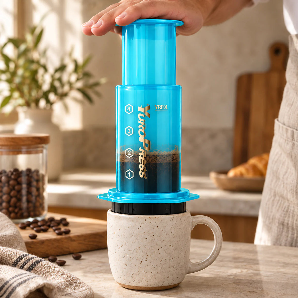 Mãos pressionam a Aeropress Cafeteira YuroPress Azul sobre uma caneca de cerâmica