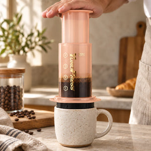 Mãos pressionam a Aeropress Cafeteira YuroPress Laranja sobre uma caneca de cerâmica