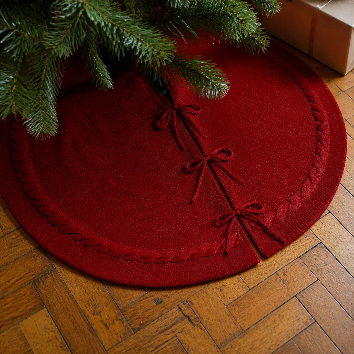 Detalhe da saia para árvore de Natal vermelha com três laços em piso de madeira
