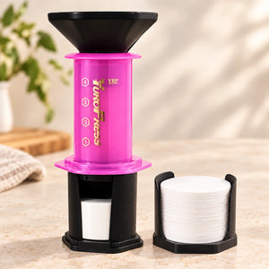 Aeropress Cafeteira YuroPress Rosa ao lado do porta-filtros e filtros de papel de 64 mm