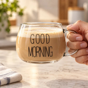 Xícara de vidro Good Morning Lumi Homi com estampa preta e bebida clara, segurada pela alça por uma mão