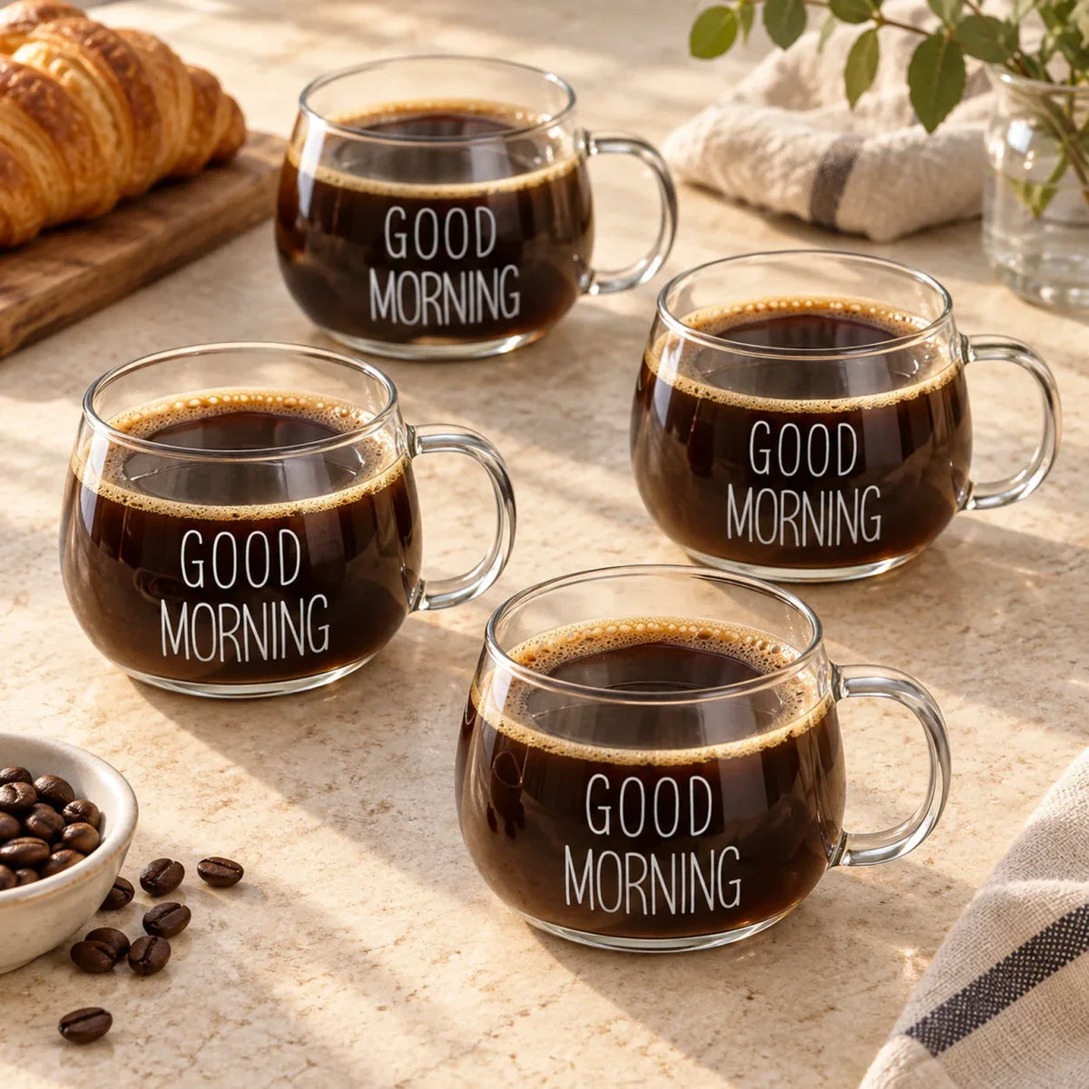 Quatro xícaras de vidro Good Morning Lumi Homi com estampa branca e café em uma mesa com croissants e grãos