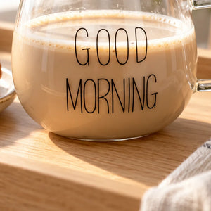 Detalhe da estampa preta Good Morning e da alça de vidro da xícara Lumi Homi com bebida clara