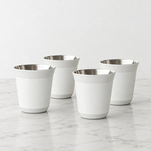 Conjunto de quatro xícaras de café inox branco Lumi Homi, com corpo afunilado e interior metálico polido, sobre bancada clara