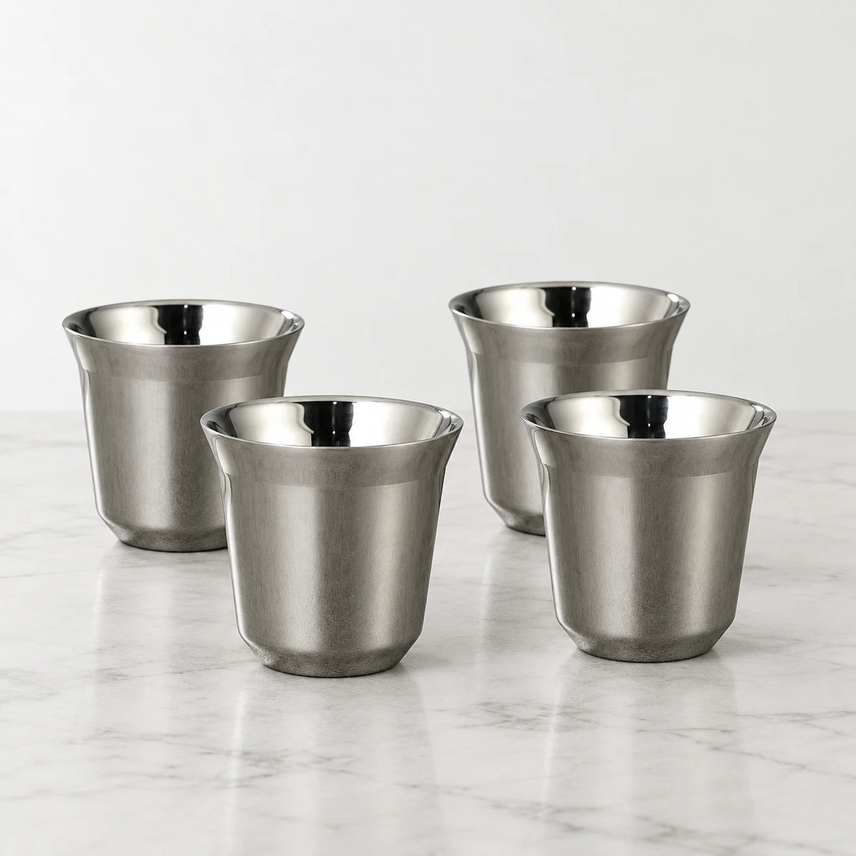 Conjunto de quatro xícaras de café inox cinza Lumi Homi, com acabamento prateado acetinado e interior polido, sobre bancada clara