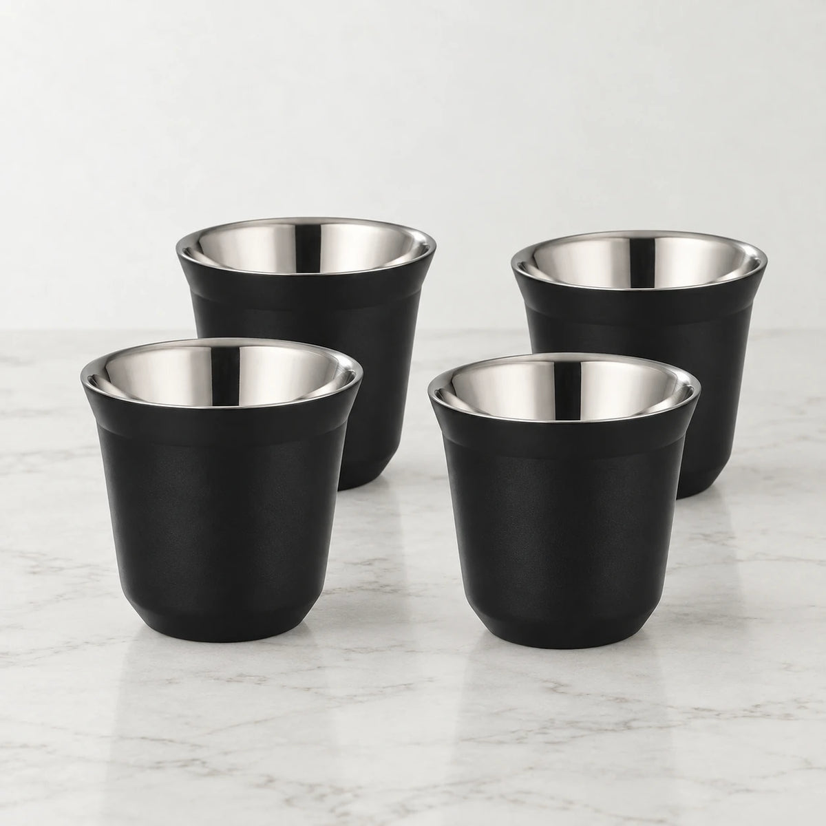 Conjunto de quatro xícaras de café inox preto Lumi Homi, vazias, com interior metálico sobre bancada clara