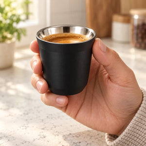 Xícara de café inox preta Lumi Homi com café, segurada por uma mão