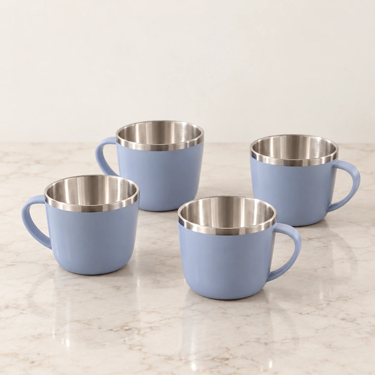 Kit com quatro xícaras azul-acinzentadas com alça e interior metálico sobre pedra clara