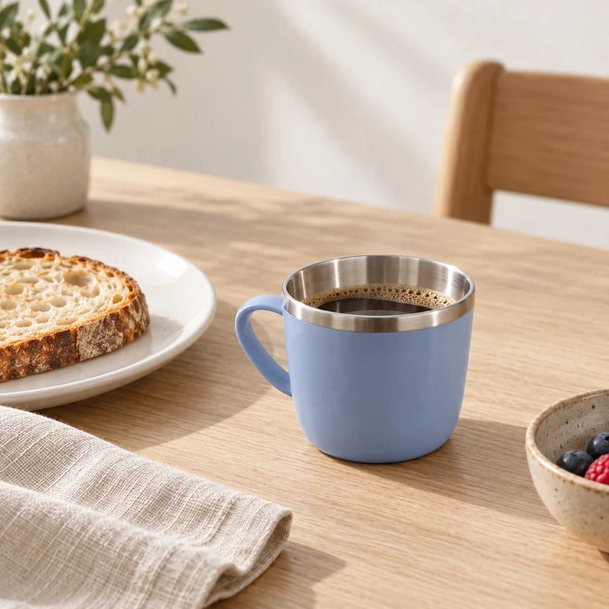 Xícara azul-acinzentada com café ao lado de pão e guardanapo de linho na mesa de café da manhã